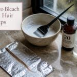 Small hair strand coated with bleach on foil beside a timer, comb and bowl
