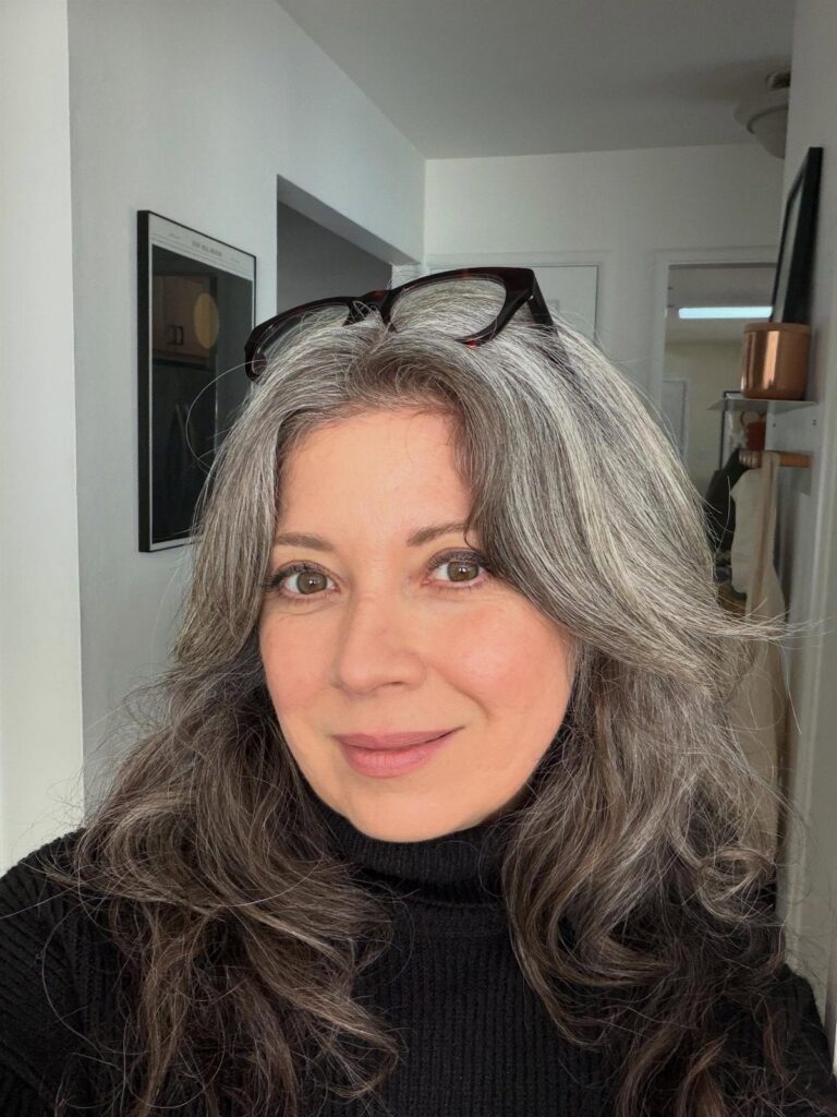 Woman with long wavy blended grey hair and glasses resting on her head