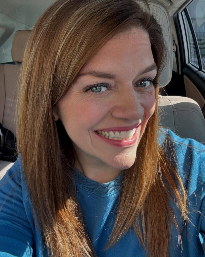 Woman with long brown hair and caramel highlights smiling in a car