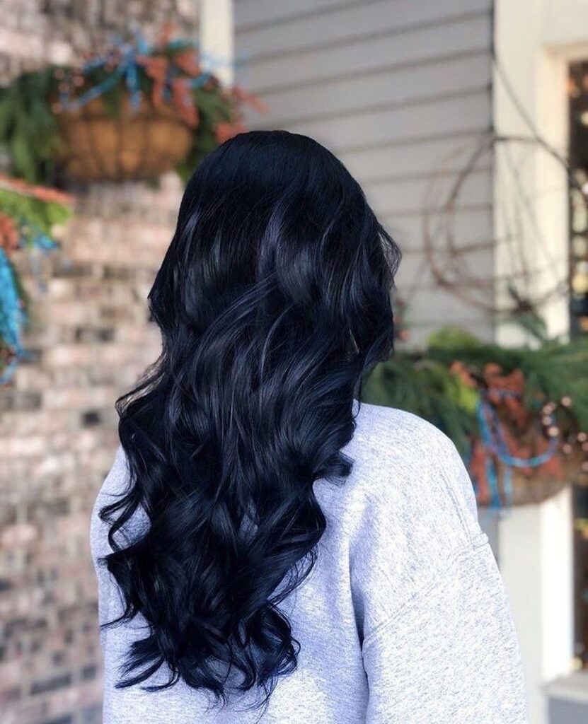 Long, wavy dark blue-black hair falls over a light gray top