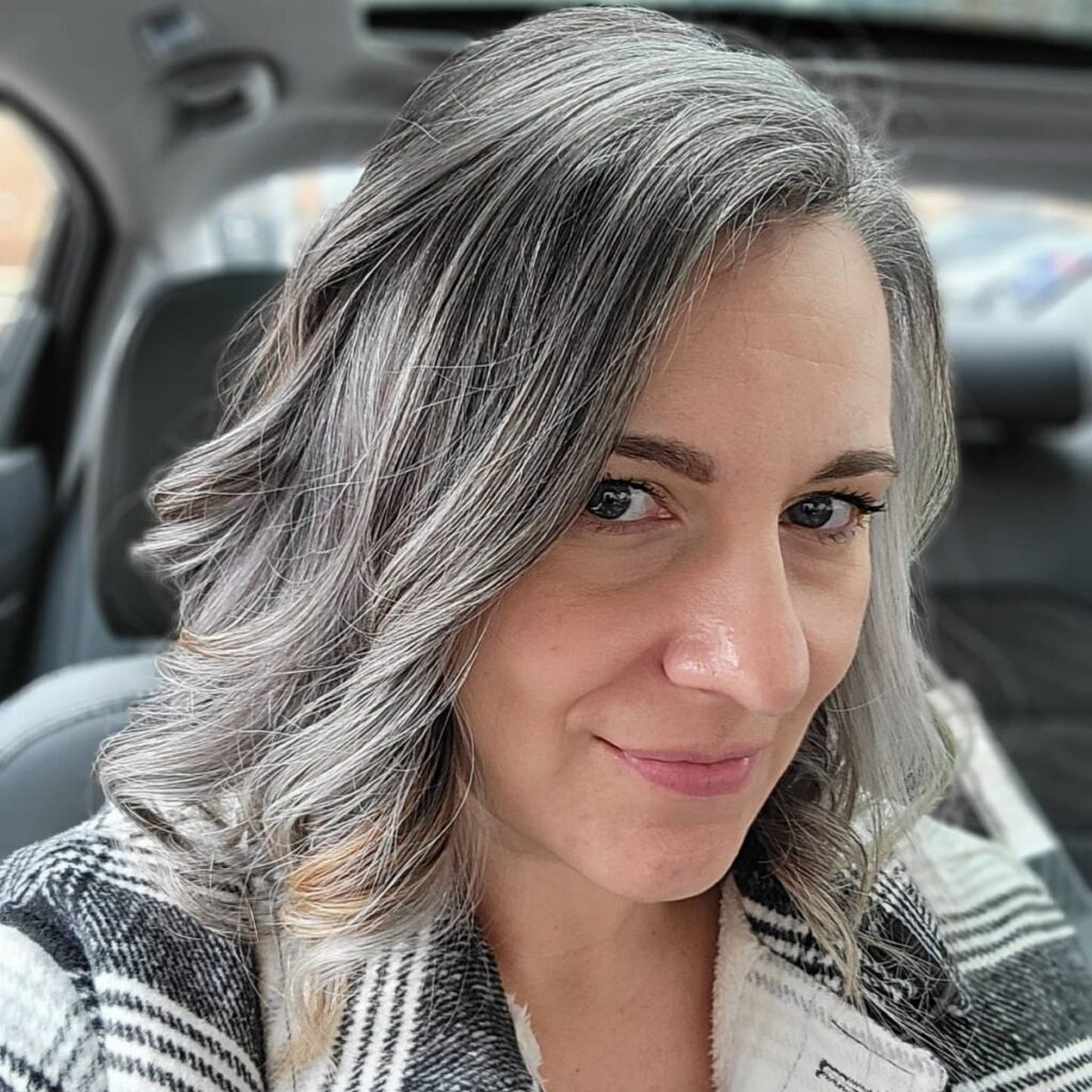Woman with long, wavy silver-gray hair posing in a car