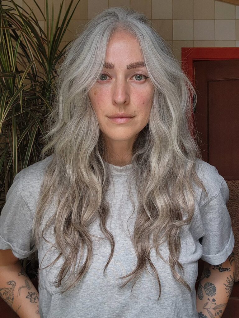 Person with long, wavy silver-gray hair wearing a light gray T-shirt