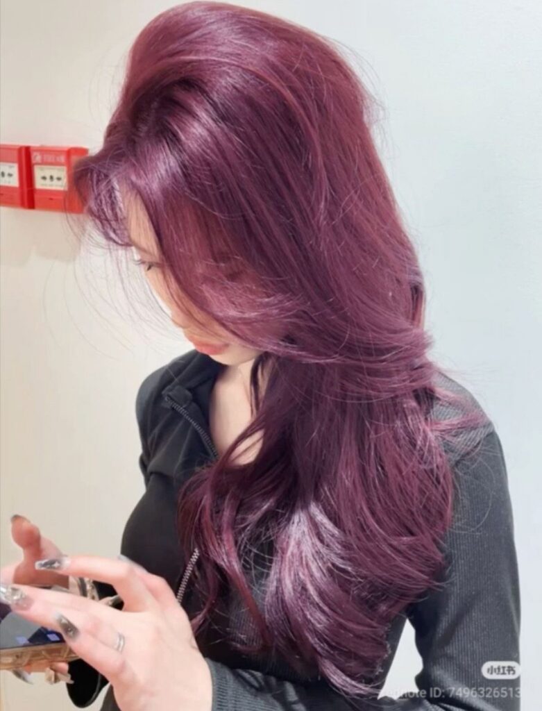 Long layered plum-purple hair frames a person looking down at their phone