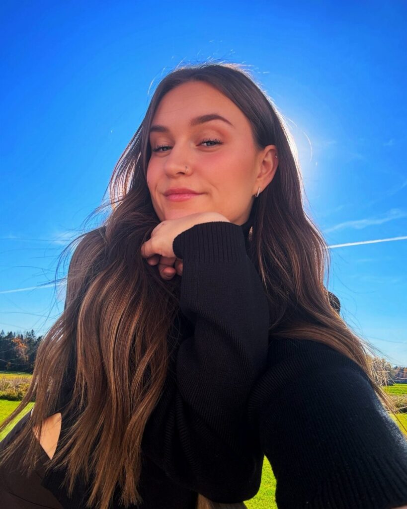 Woman with long wavy brown hair posing outdoors beneath a bright blue sky
