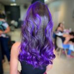 Long curled brown hair with vivid purple color in a salon