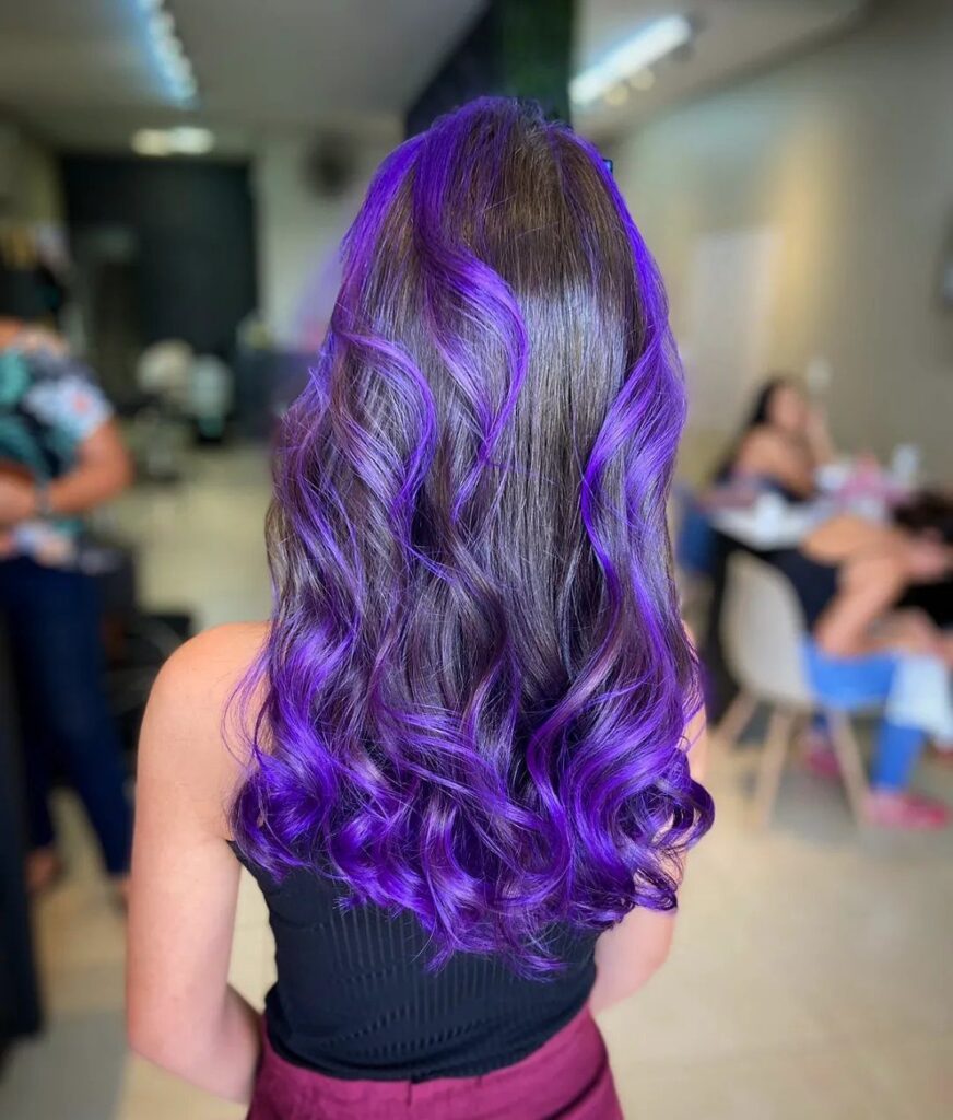 Long curled brown hair with vivid purple color in a salon