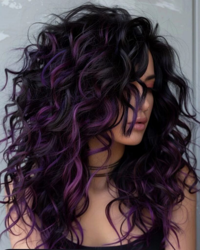 Long curly black hair with vivid purple streaks frames a person's face