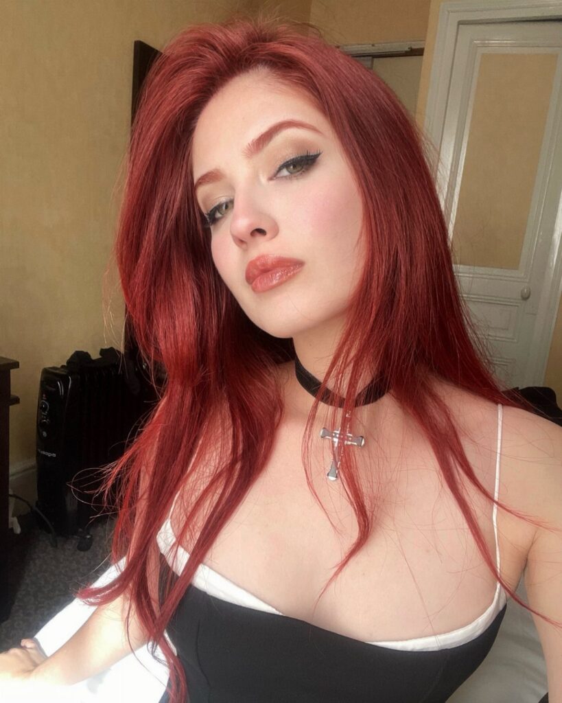 Woman showcasing long vivid red hair with dark roots indoors
