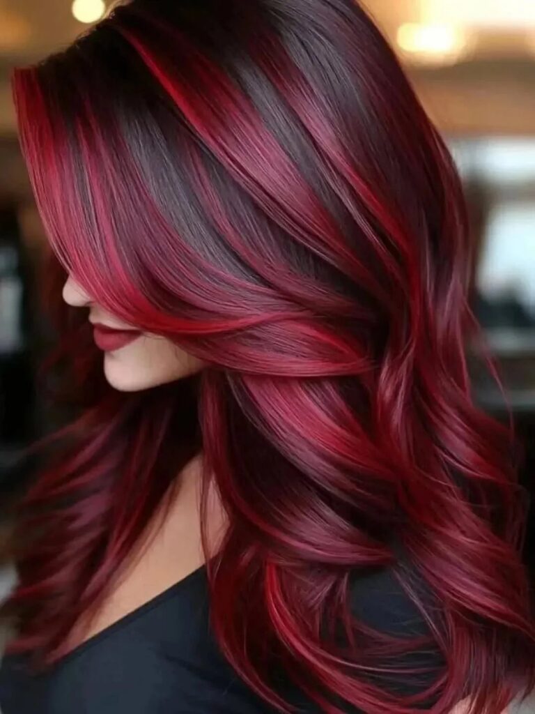 Woman showing long, layered burgundy hair with vivid red highlights